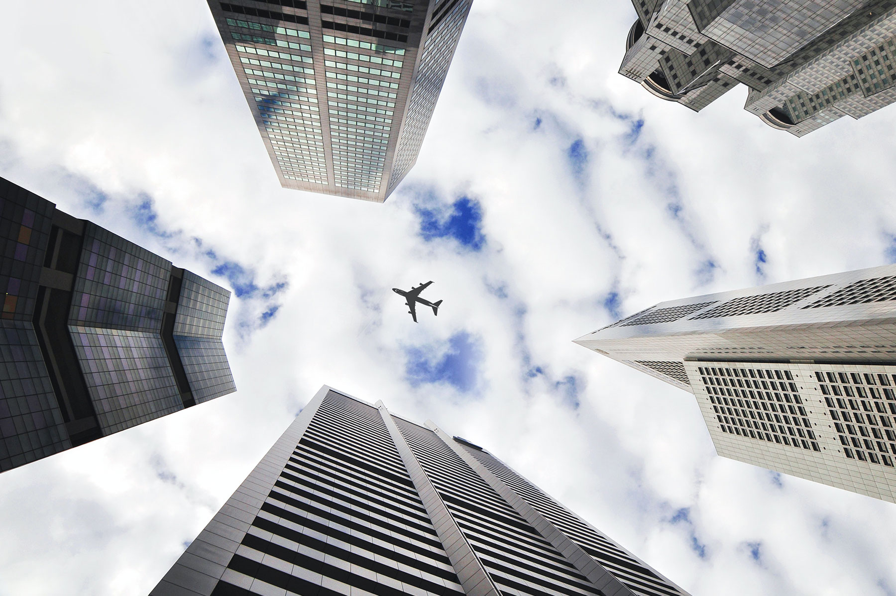 airplane flying through sky framed by skyscrapers