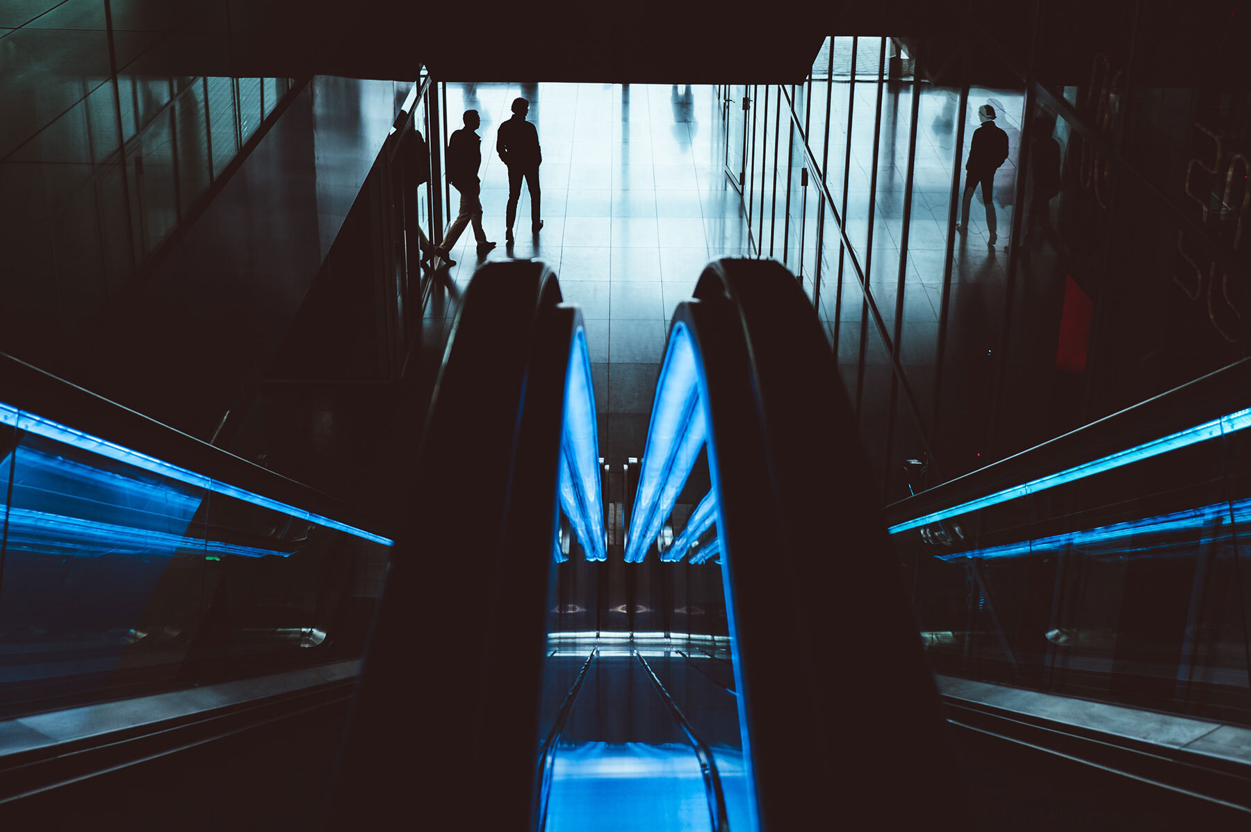 Escalator going down with silhouette of people in the background